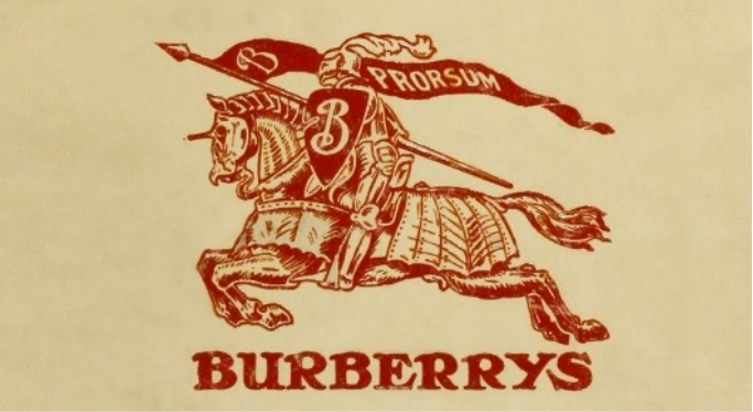 Historic Burberrys logo featuring the Equestrian Knight emblem holding a “Prorsum” banner, symbolising forward motion and the brand’s heritage identity. The vintage artwork appears in red on a beige background.