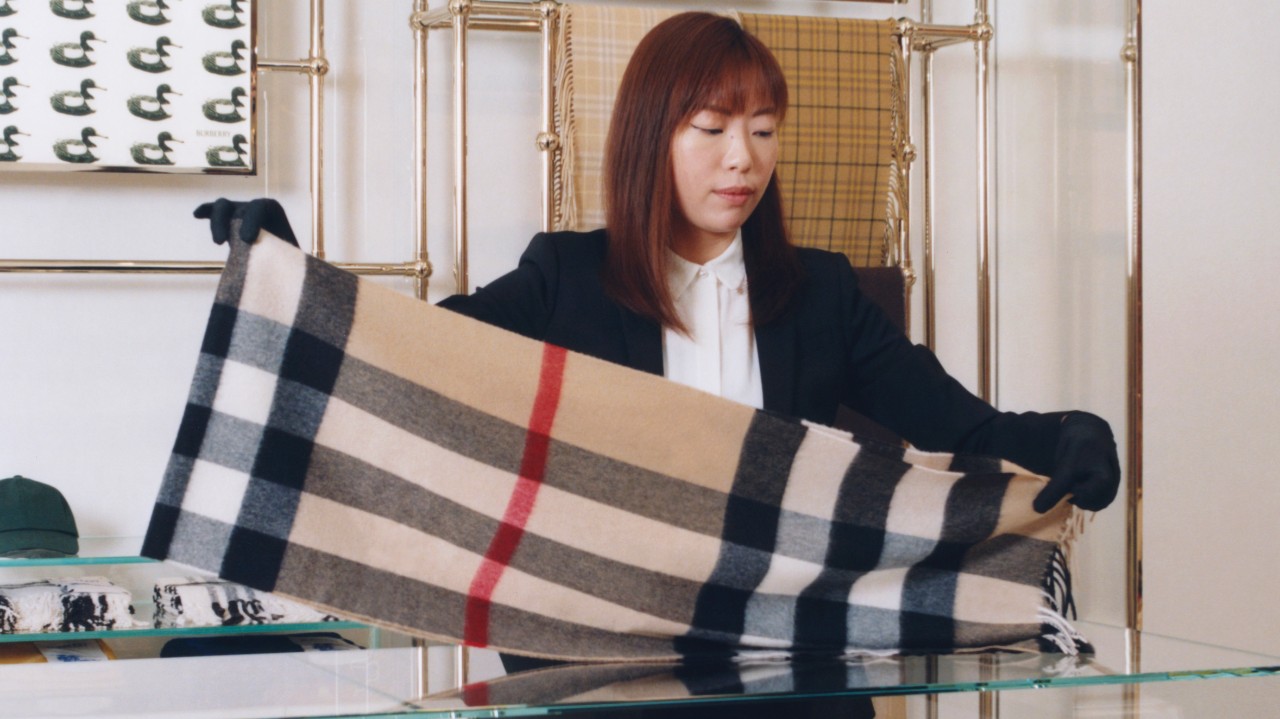 A team member carefully presenting a signature checked scarf, reflecting dedication to quality and timeless design.