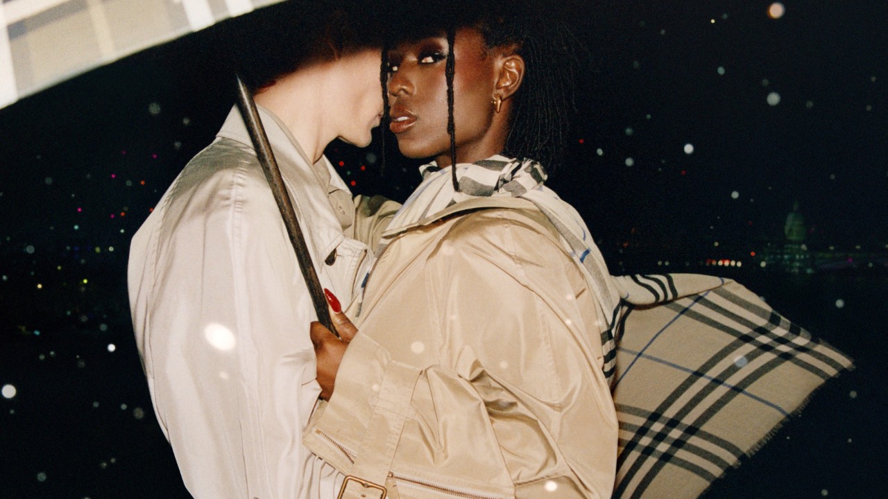 Models wearing Burberry outerwear and holding a signature Burberry check umbrella on a rainy night.