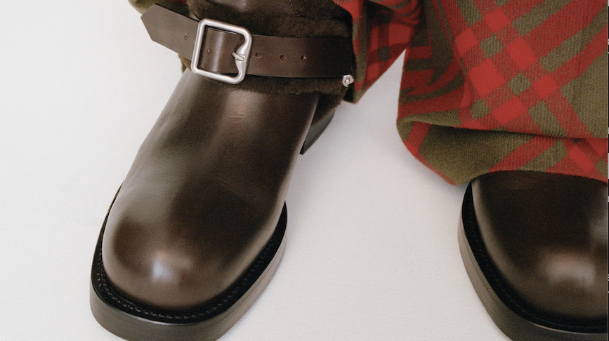 Close-up of brown leather boots with buckle straps beneath red and green Burberry check trousers.