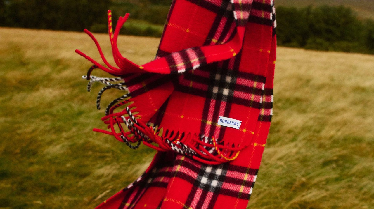 A Burberry cashmere scarf with the iconic red check pattern blowing in the wind, symbolising British heritage, craftsmanship, and timeless elegance.