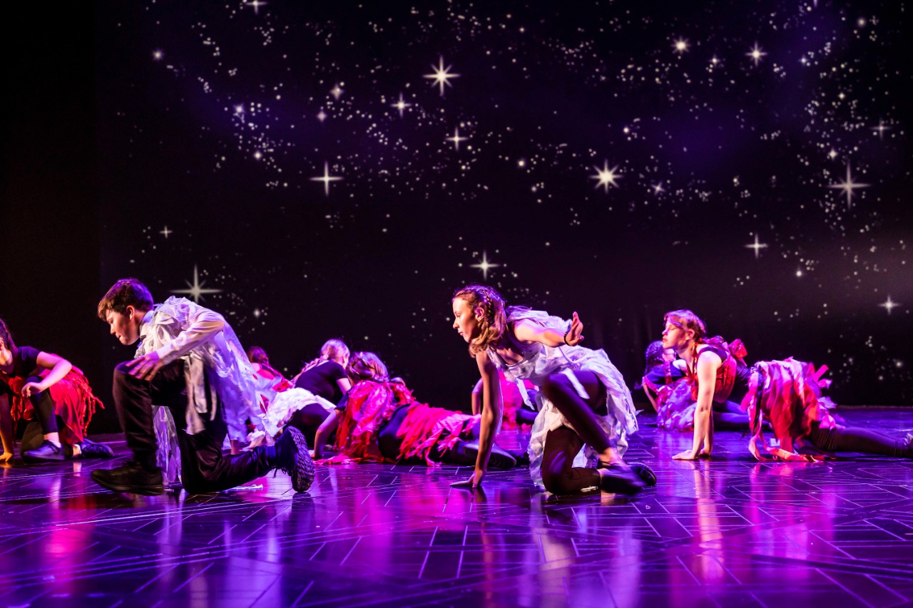 A group of young performers on stage under star-like lighting alongside an introduction to The Burberry Foundation, an independent charity focused on creativity, positive community impact, and building a sustainable future for young people.