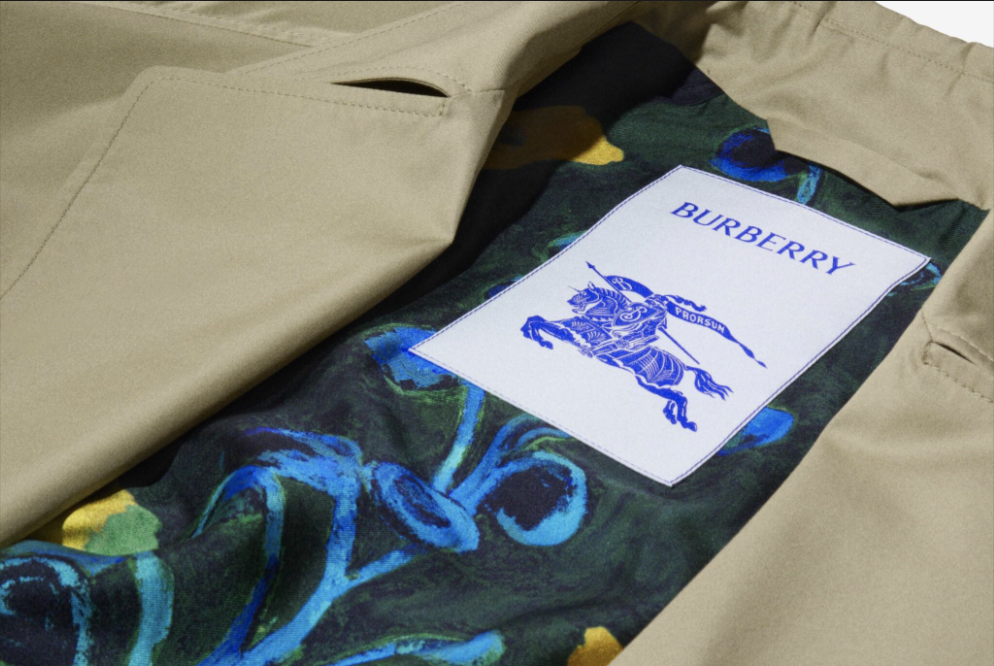Close-up of the inside of a beige Burberry coat showing a colourful patterned lining and a white label with the Burberry knight logo in blue, representing the brand’s commitment to codes and policies.