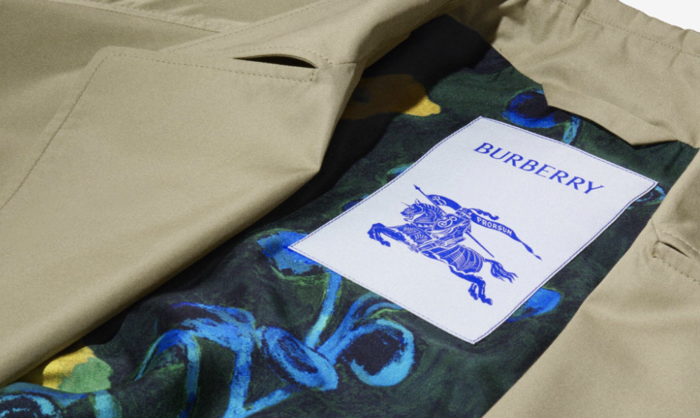 Close-up of the inside of a beige Burberry coat showing a colourful patterned lining and a white label with the Burberry knight logo in blue, representing the brand’s commitment to codes and policies.