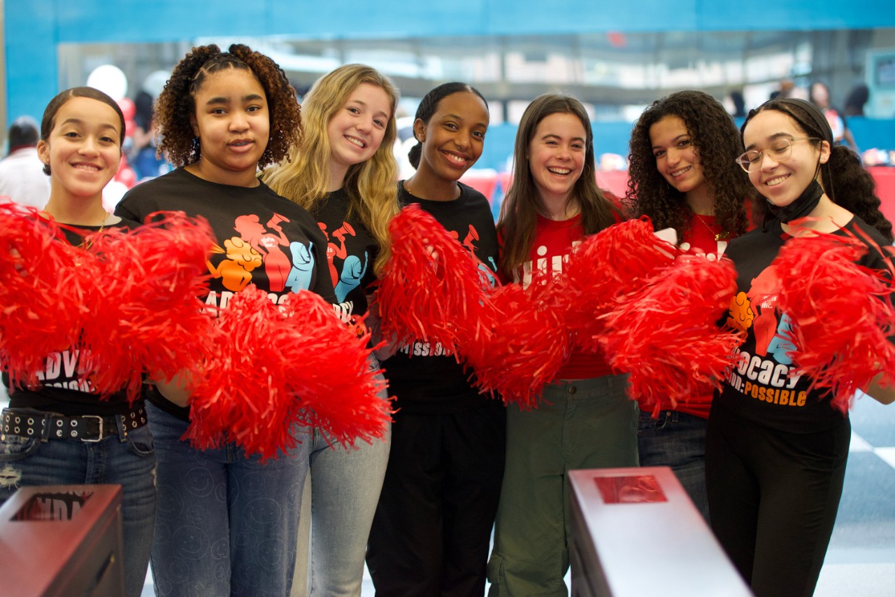 A group of young people smiling and holding red cheer pom-poms while participating in a Girls Inc. of New York City event.