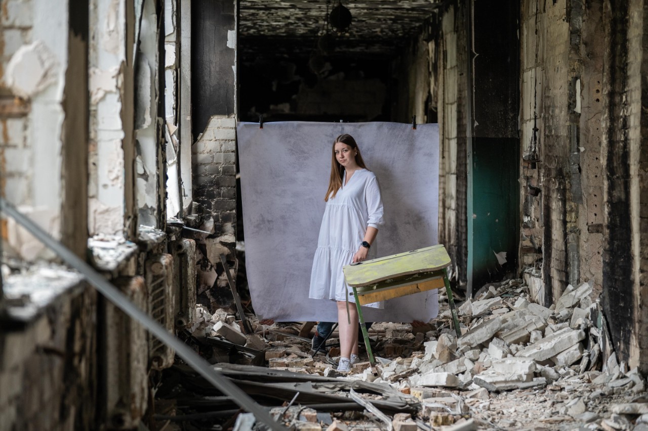 A young person stands in a damaged, debris-filled building holding a suitcase, symbolising the challenges faced by displaced youth and the humanitarian support provided through the partnership between the Burberry Foundation and Save the Children.