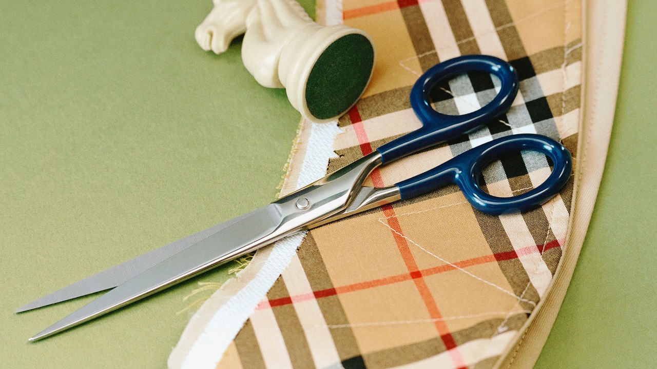 Burberry check fabric with blue-handled scissors cutting along the edge.